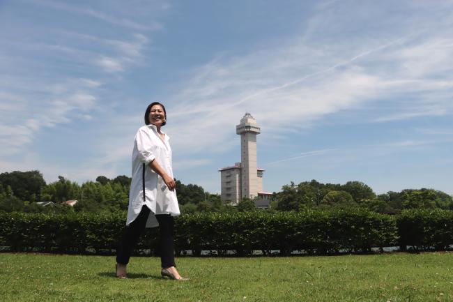 スカイワードあさひが見える長池周辺をふるさと大使のあおきさやかさんがさわやかに歩く様子